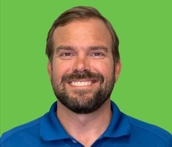 Man in blue shirt in front of green background.