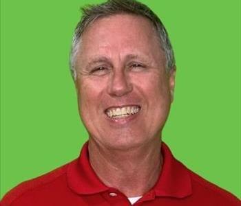 Smiling man in red shirt in front of green background.