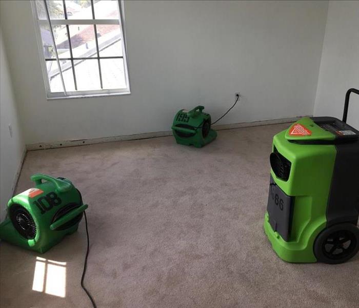 Green air movers and dehumidifiers set up and running on the floor in an empty room.